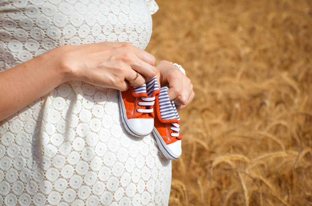 An expectant woman holding baby shoes